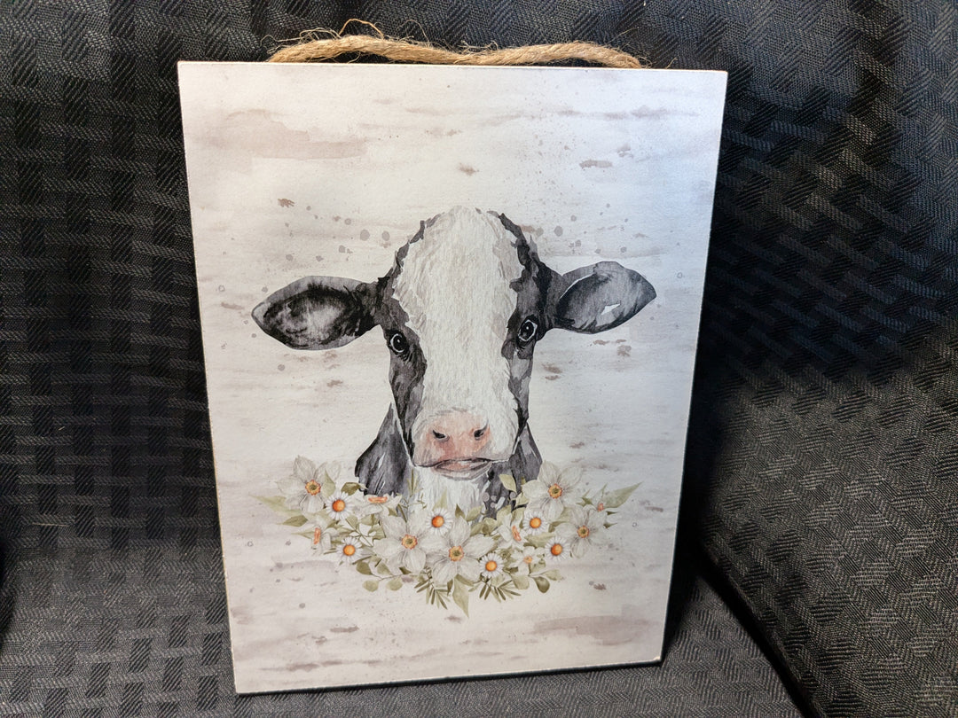 Charming hanging sign featuring a cow surrounded by flowers, perfect for rustic decor.