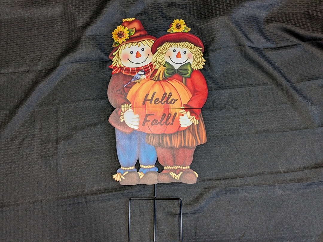 Hello Fall' scarecrow stake – charming readymade craft featuring a whimsical scarecrow design alongside a white pumpkin plaid block and orange pumpkin plaid block. Perfect for autumn outdoor decor, adding a festive touch to your garden or porch.